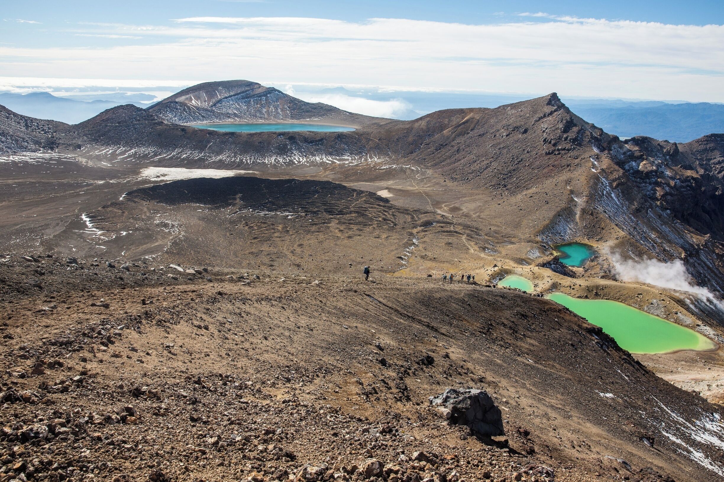 A rugged mountain landscape with multiple green lakes and a person hiking.