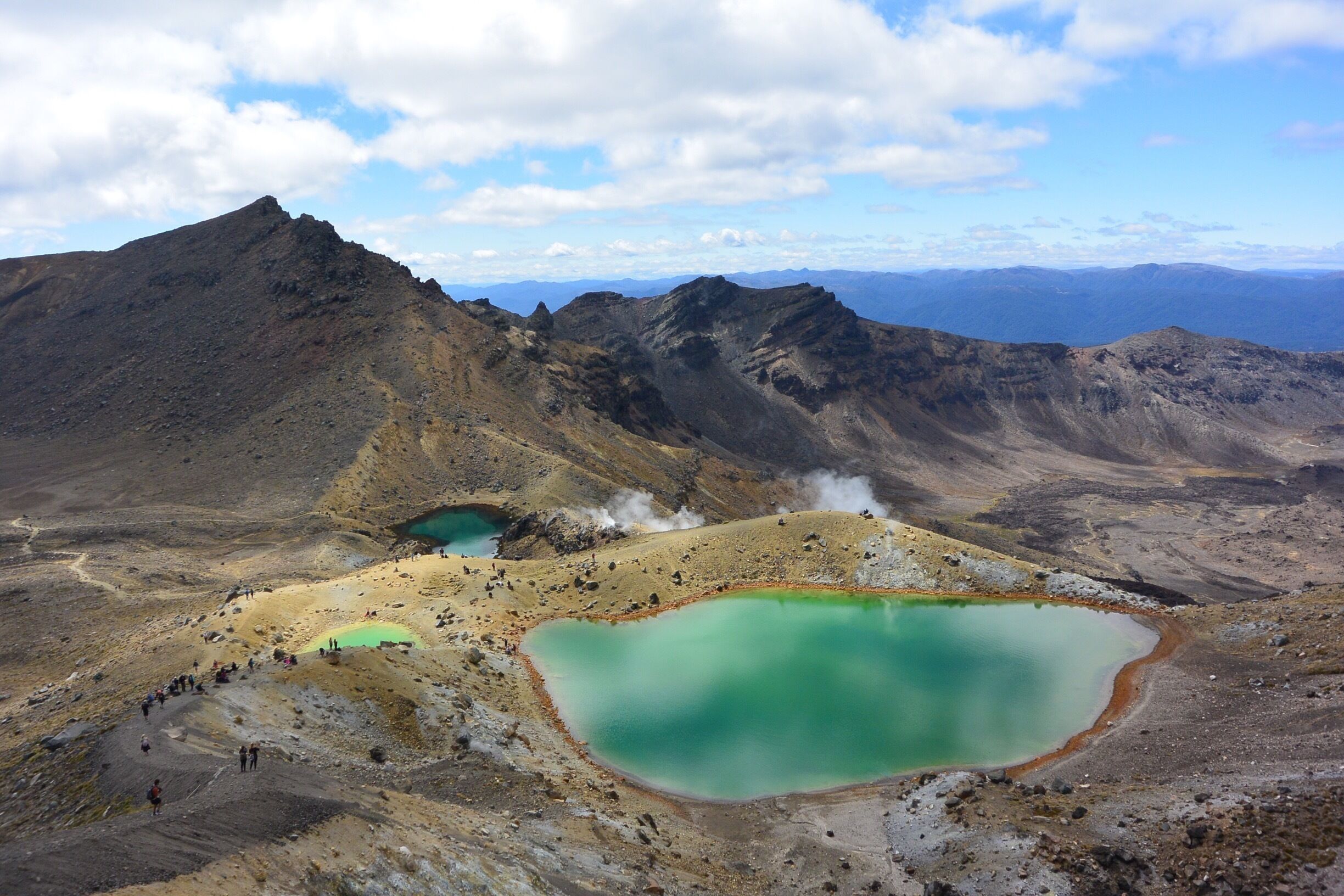 A mountainous landscape with two turquoise lakes surrounded by rocky terrain and a group of hikers.