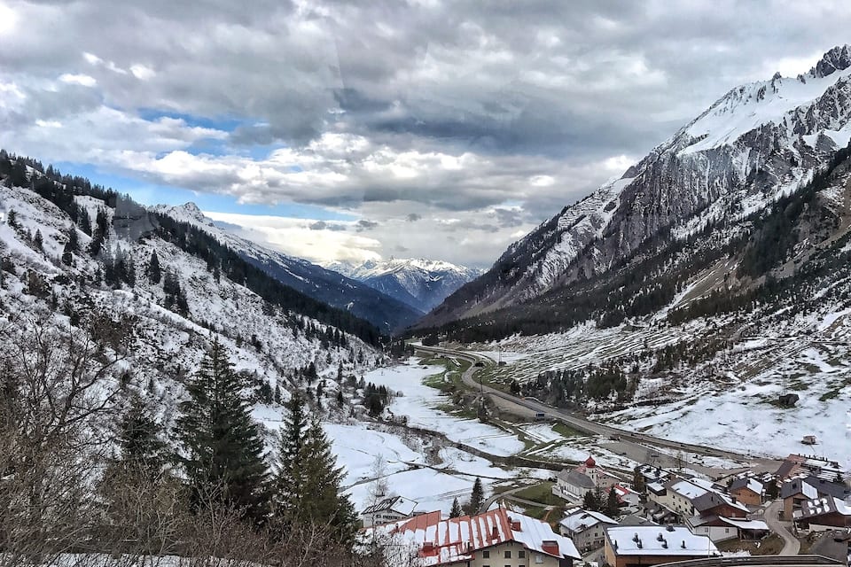 A snow-covered valley with mountains, a winding road, and a small village with traditional houses.