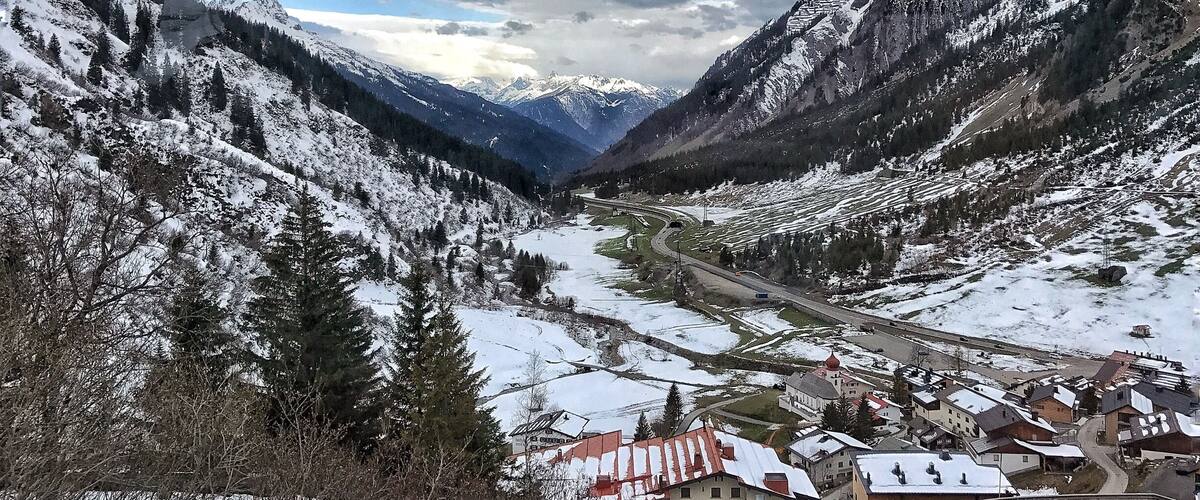 A snow-covered valley with mountains, a winding road, and a small village with traditional houses.