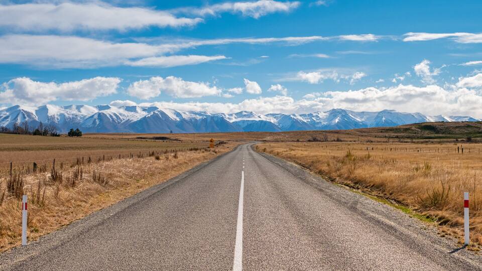 A gravel road leading to snow-capped mountains under a clear sky.