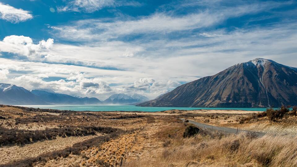 A mountainous landscape with a clear sky, a turquoise lake, and a dirt road.