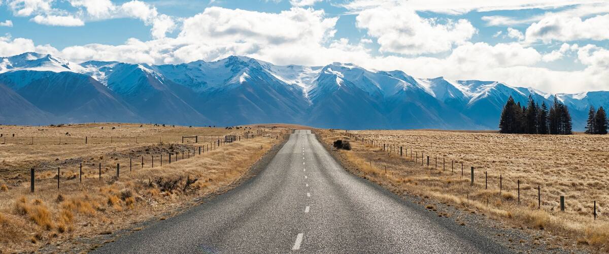 A road leading to snow-capped mountains with a clear sky.