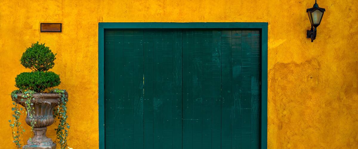 A yellow wall with a green door and a small tree on a pedestal.