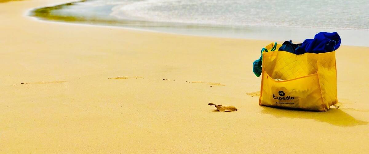 A yellow bag with blue items on a sandy beach with ocean waves in the background.