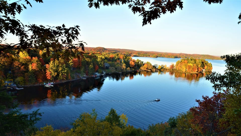 A calm lake surrounded by autumn-colored trees and a small house on the shore.