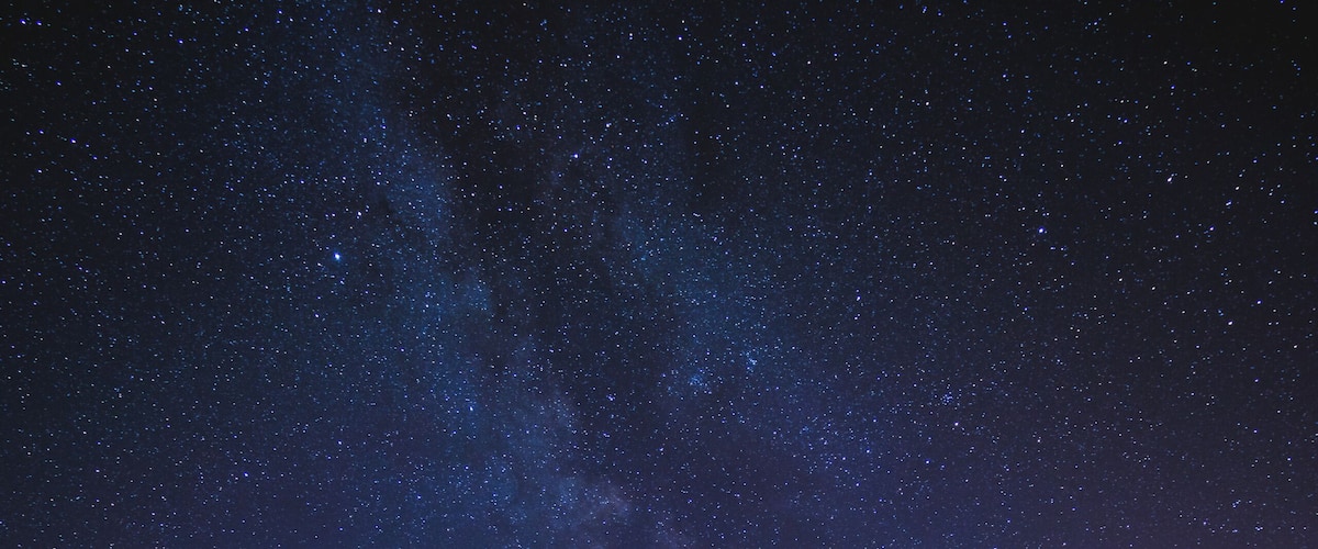 A night sky with stars and the Milky Way over a calm body of water with a wooden dock.