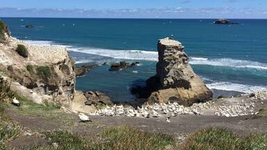 A coastal landscape with a prominent rock formation, a sandy beach, and the ocean.