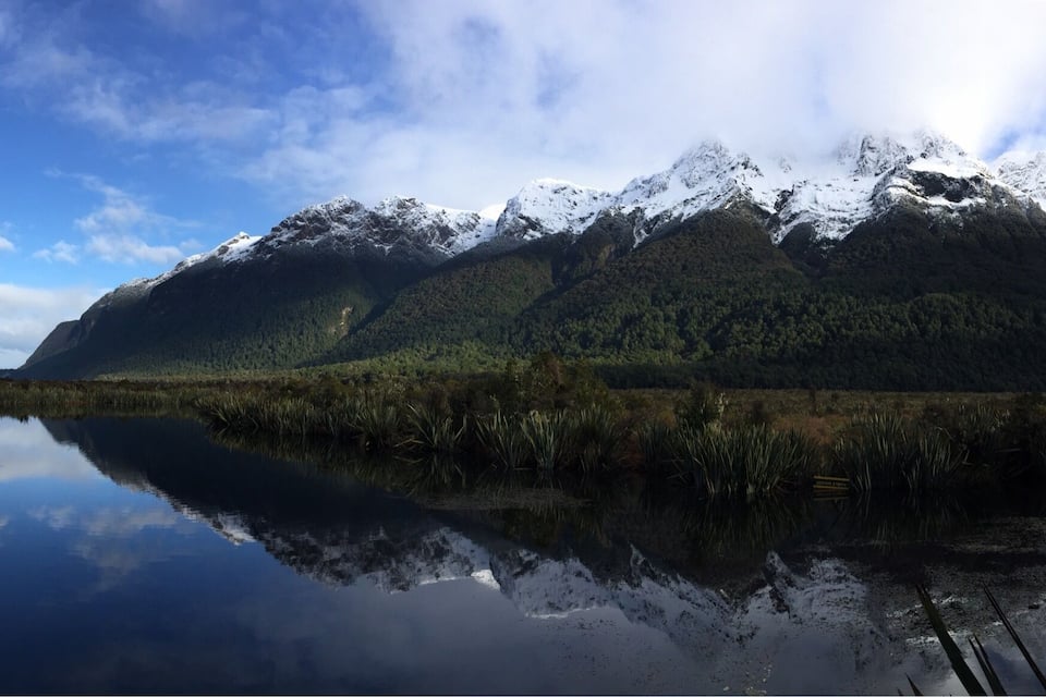 Une chaîne de montagnes aux sommets enneigés et un lac paisible qui reflète le paysage.