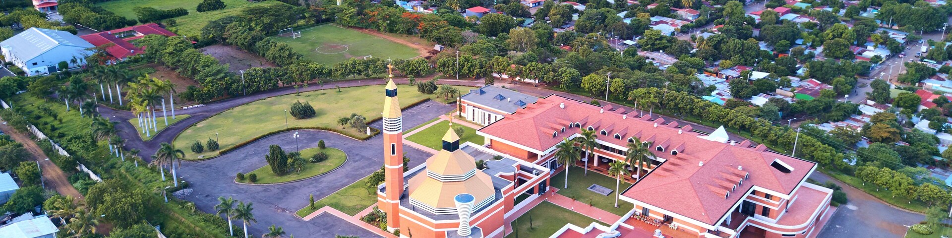 Vista aérea de un paisaje urbano con una mezquita destacada, que presenta un minarete alto y una cúpula, rodeada de zonas residenciales y vegetación.