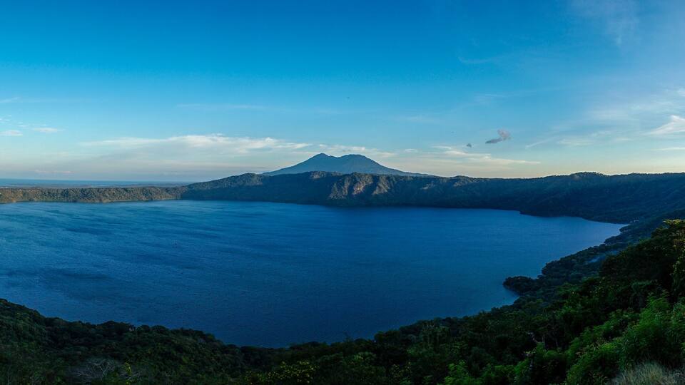 A large lake surrounded by forested hills and a mountain in the distance.