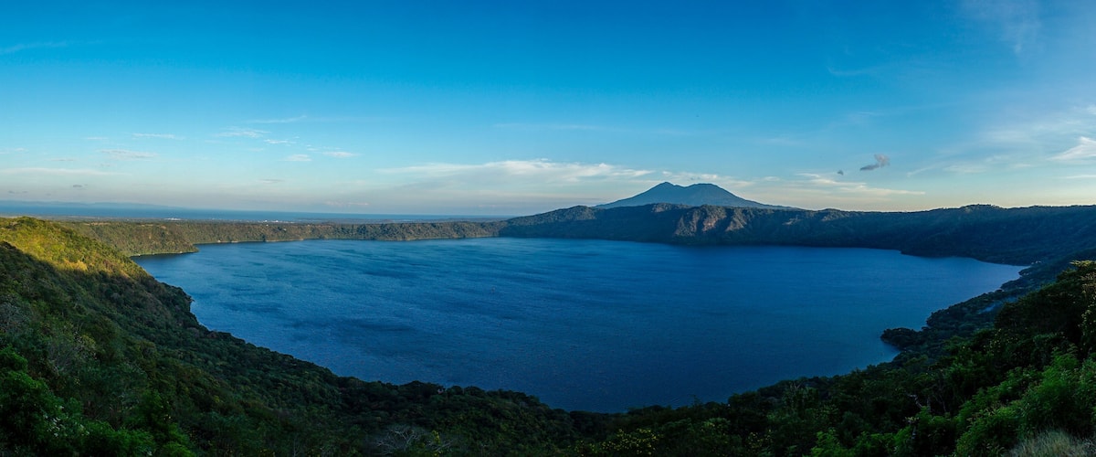 A large lake surrounded by forested hills and a mountain in the distance.