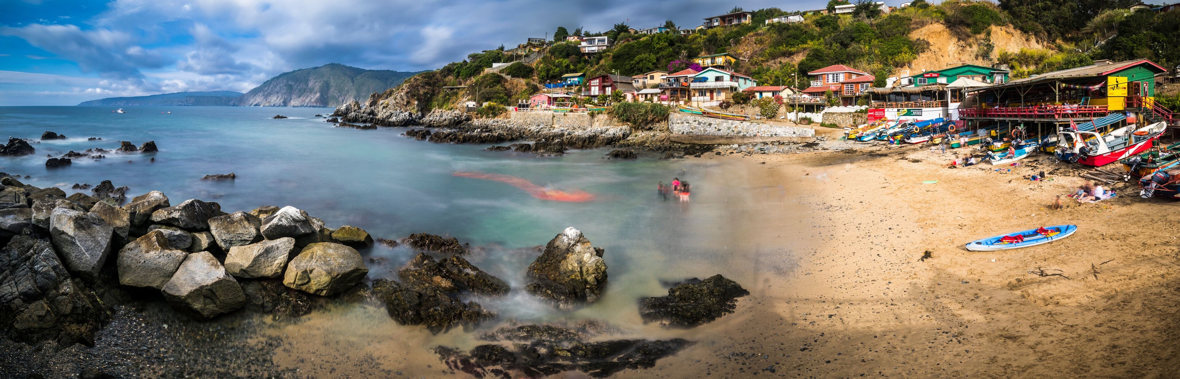 A coastal beach with rocky shores, colorful houses, and boats.