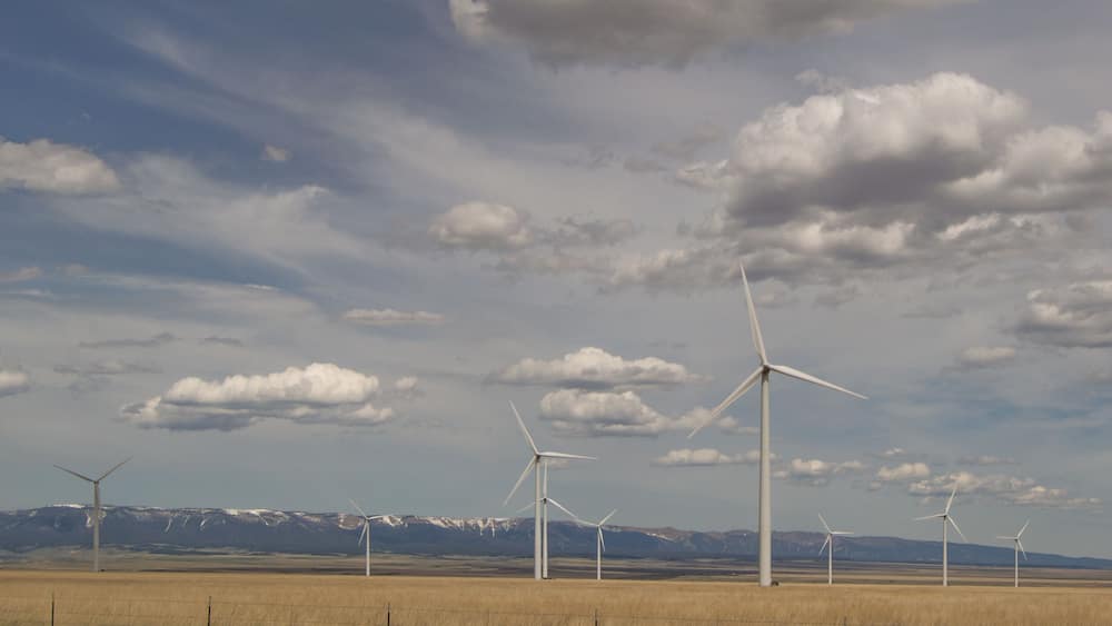 Judith Gap windmills that are part of a large renewable energy wind farm with mountains in the background, prairie in the foreground and cloudy skies above.