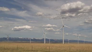 Judith Gap windmills that are part of a large renewable energy wind farm with mountains in the background, prairie in the foreground and cloudy skies above.
