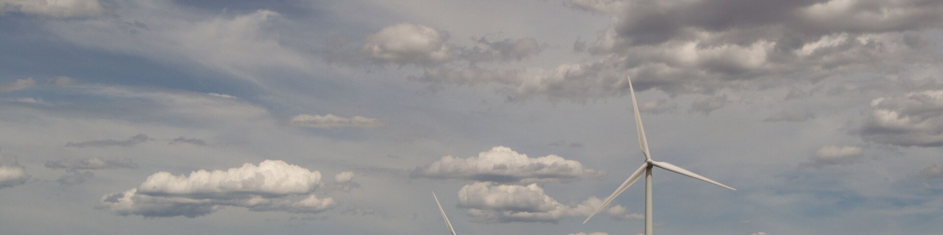 Judith Gap windmills that are part of a large renewable energy wind farm with mountains in the background, prairie in the foreground and cloudy skies above.