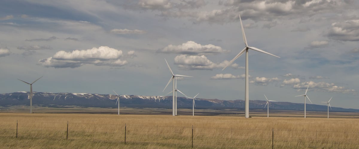Judith Gap windmills that are part of a large renewable energy wind farm with mountains in the background, prairie in the foreground and cloudy skies above.
