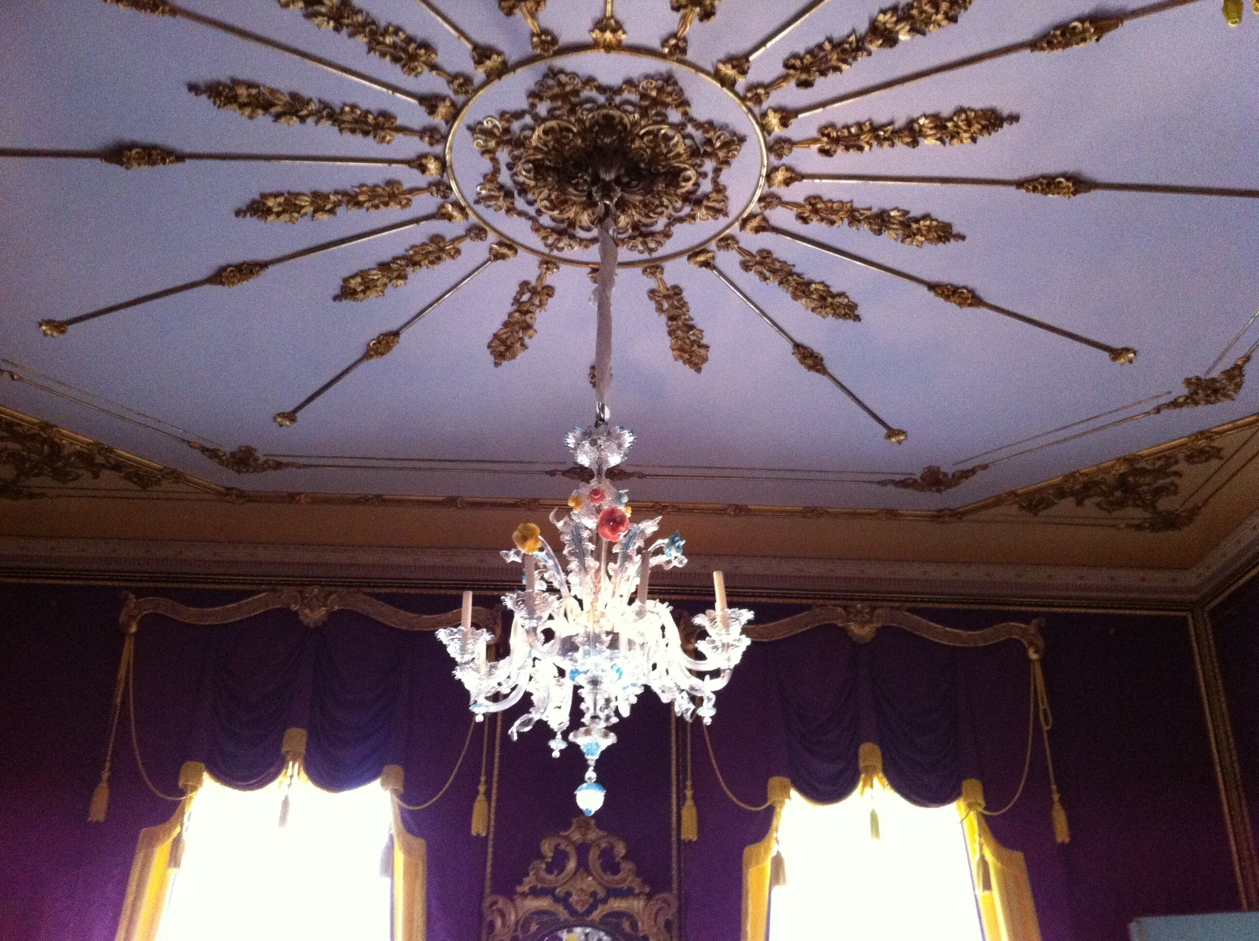 A chandelier with a central ornate design and multiple arms, hanging from a ceiling with a sunburst pattern.