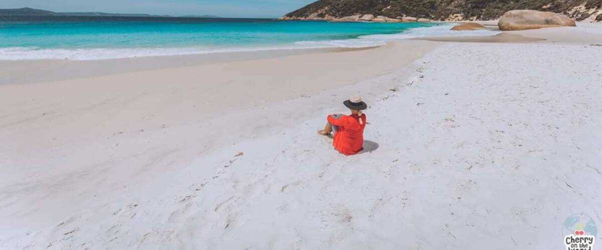 A beach with white sand, turquoise water, and rocky hills in the background.