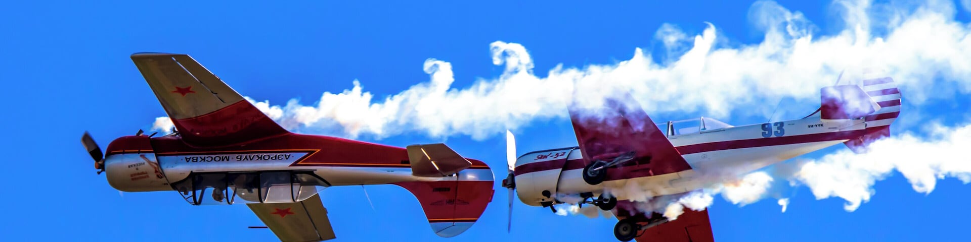 Two airplanes flying side by side with smoke trails against a clear blue sky.