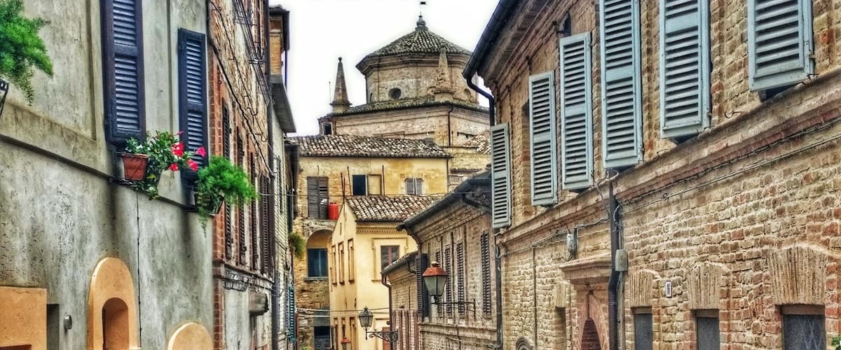 A narrow cobblestone street flanked by historic buildings with arched doorways and shutters.