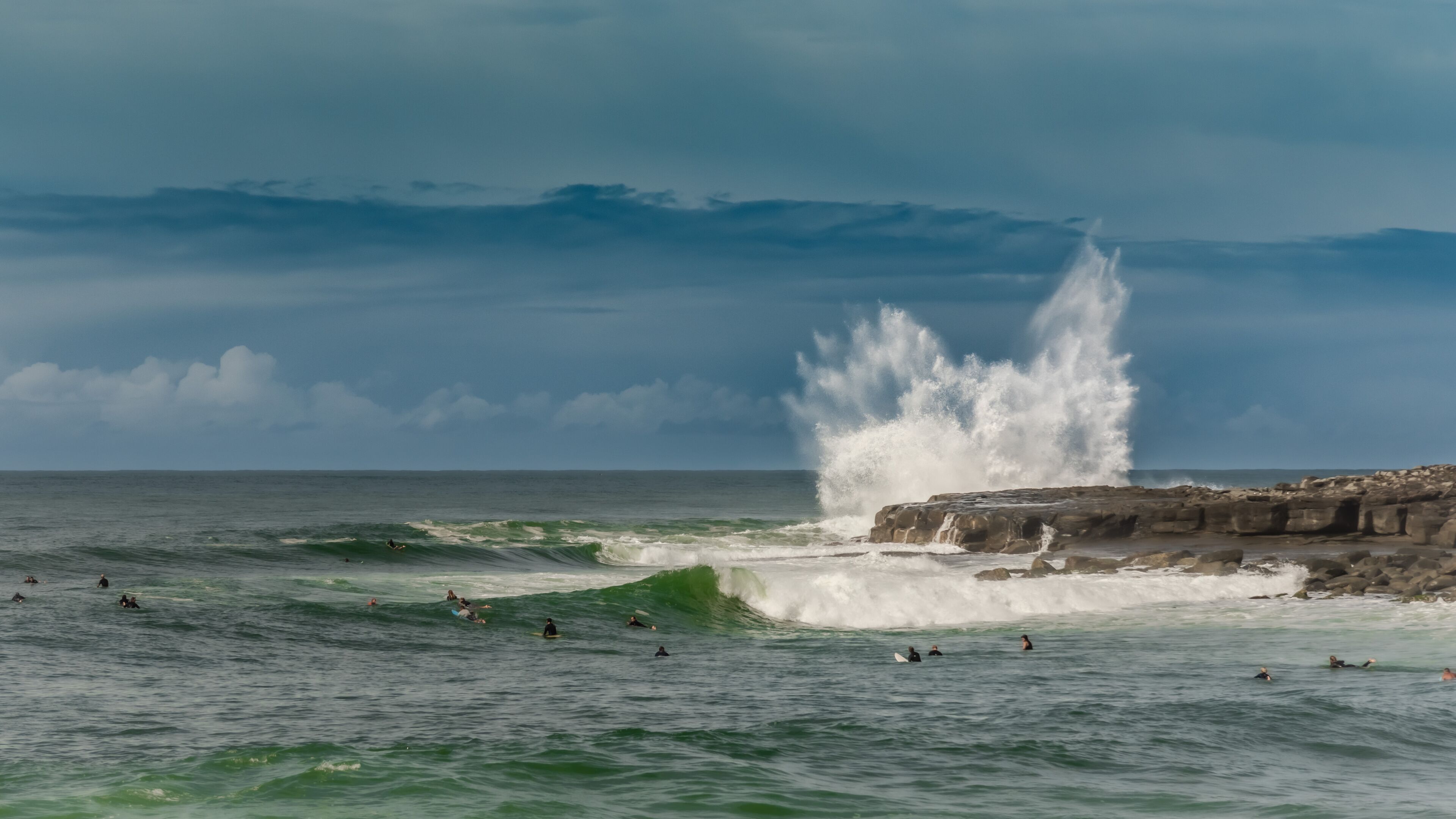A rocky coastline with waves crashing against it and surfers in the water.
