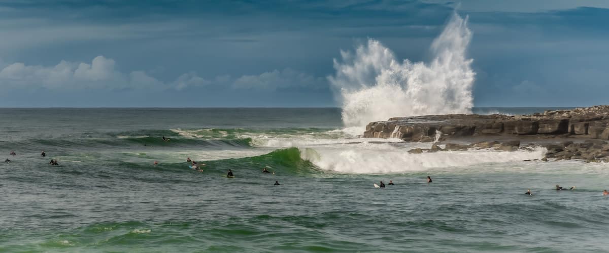 A rocky coastline with waves crashing against it and surfers in the water.