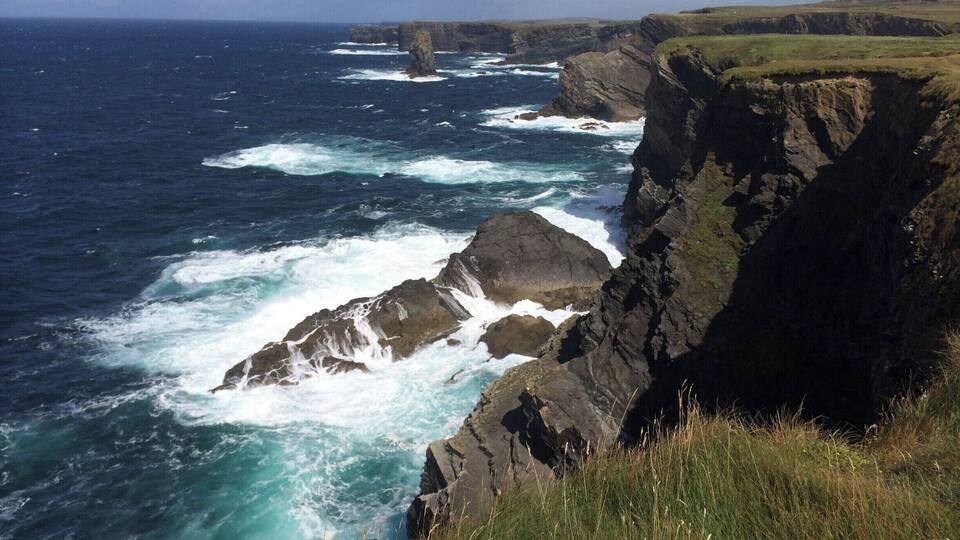 A rugged coastline with steep cliffs and turbulent sea waves crashing against the rocks.