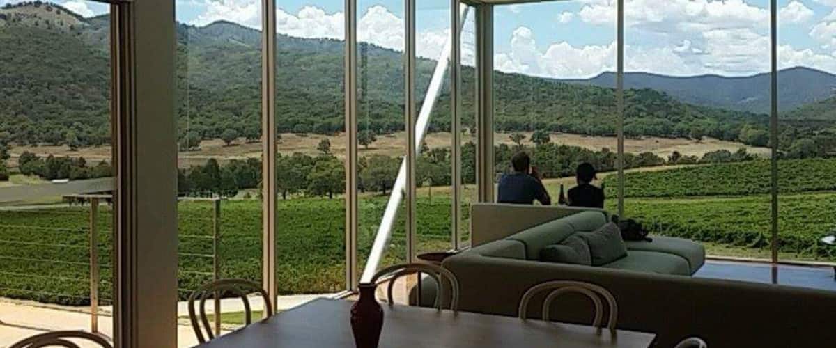 A modern interior with large windows overlooking a vineyard and distant mountains.