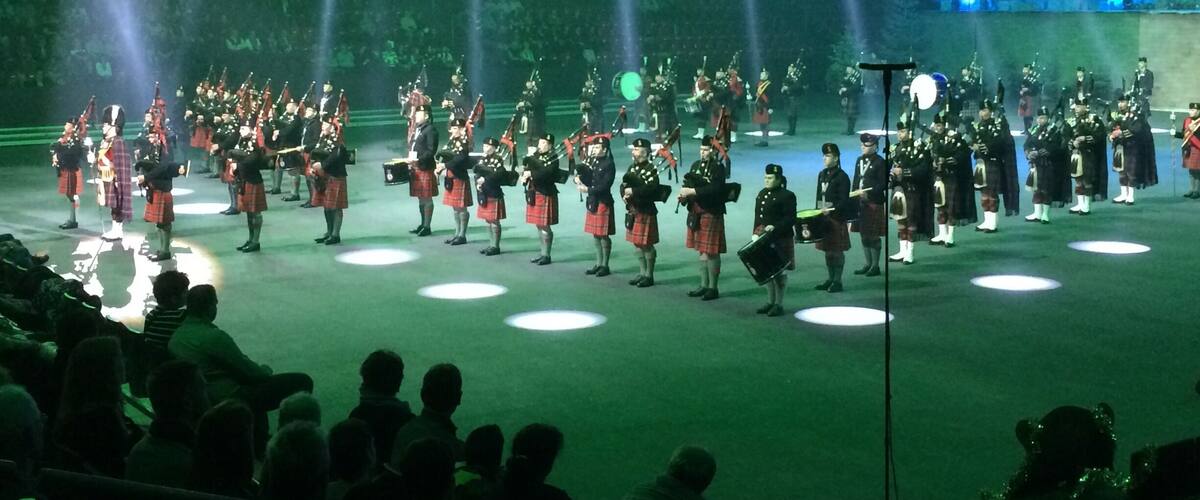 A formal event with a large group of people in kilts and military uniforms performing on a stage with spotlights.