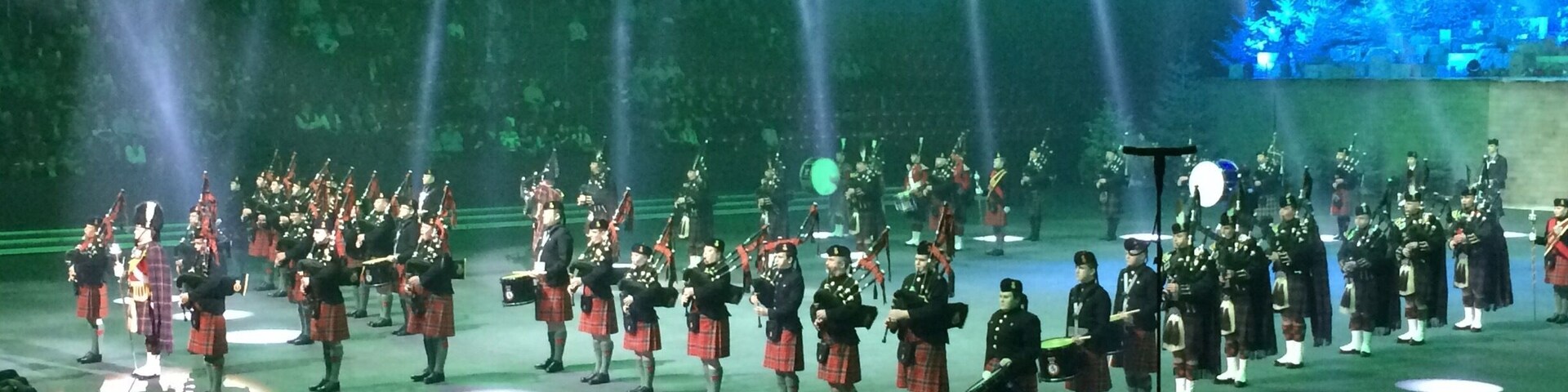 A formal event with a large group of people in kilts and military uniforms performing on a stage with spotlights.