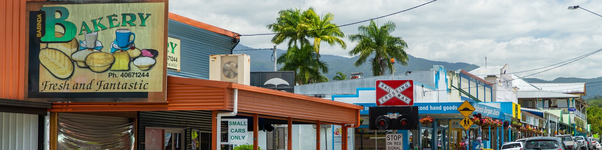 Uma rua com uma padaria, uma farmácia e uma placa de cruzamento.