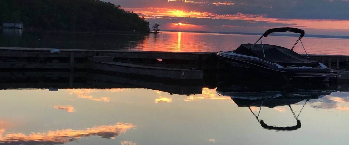 A sunset over a calm lake with a dock and a boat.