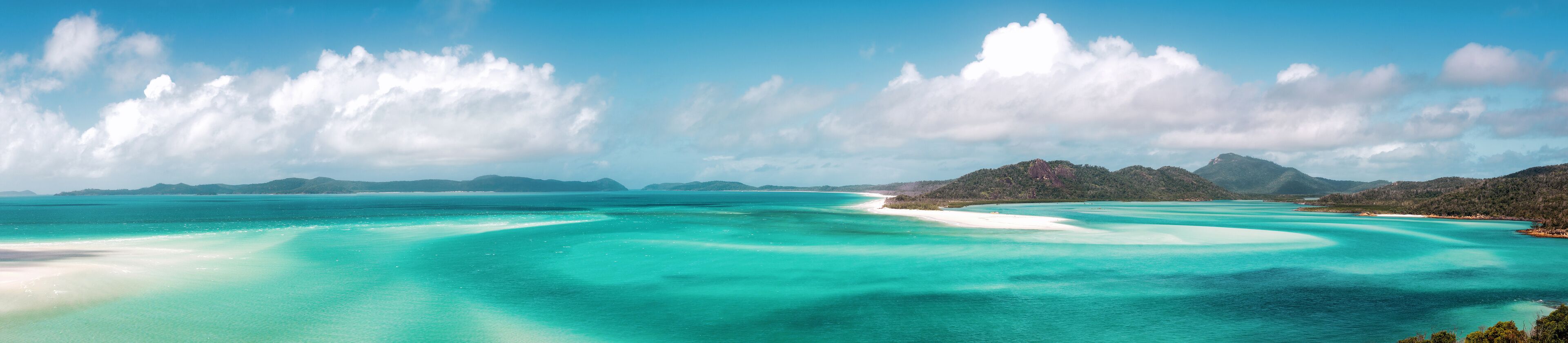 A turquoise sea with white sand beaches and distant mountains.