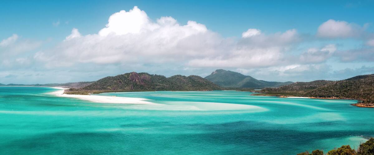 A turquoise sea with white sand beaches and distant mountains.