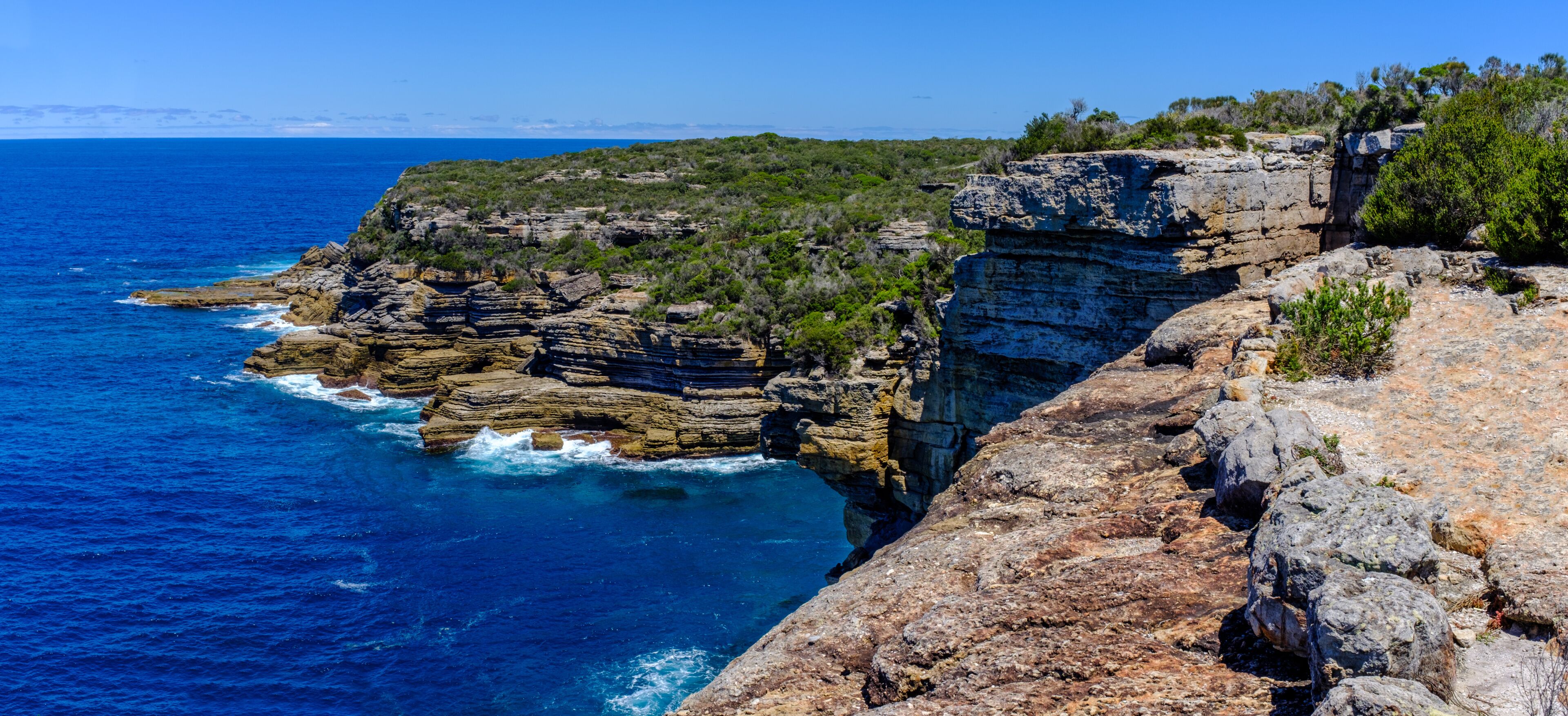 A coastal cliff with layered rock formations and a clear blue sea.