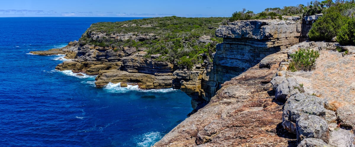 A coastal cliff with layered rock formations and a clear blue sea.