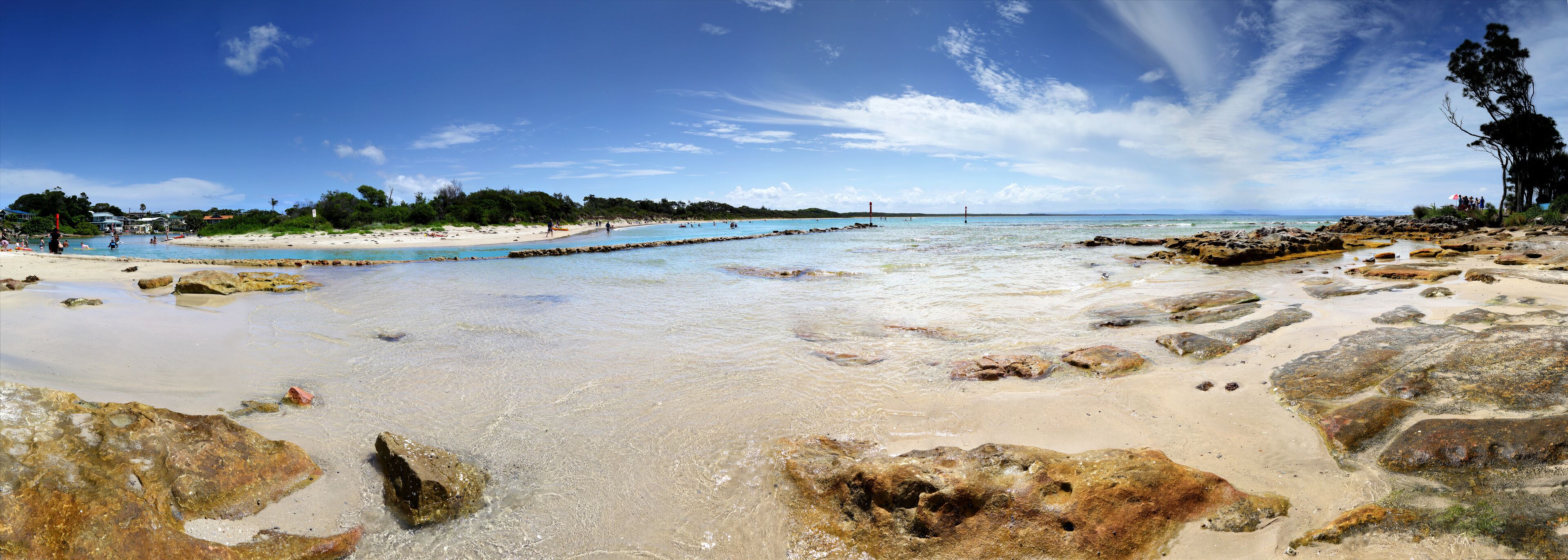 A beach with clear water, rocks, and a distant shoreline.