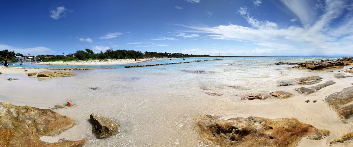 A beach with clear water, rocks, and a distant shoreline.