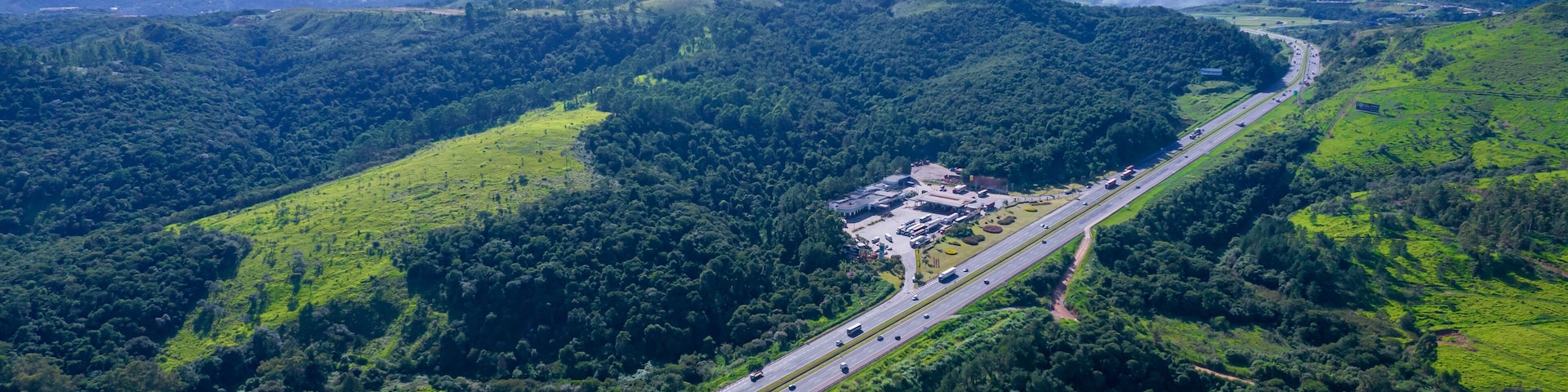 Una carretera serpentea por un valle verde exuberante, con una cadena montañosa a lo lejos.