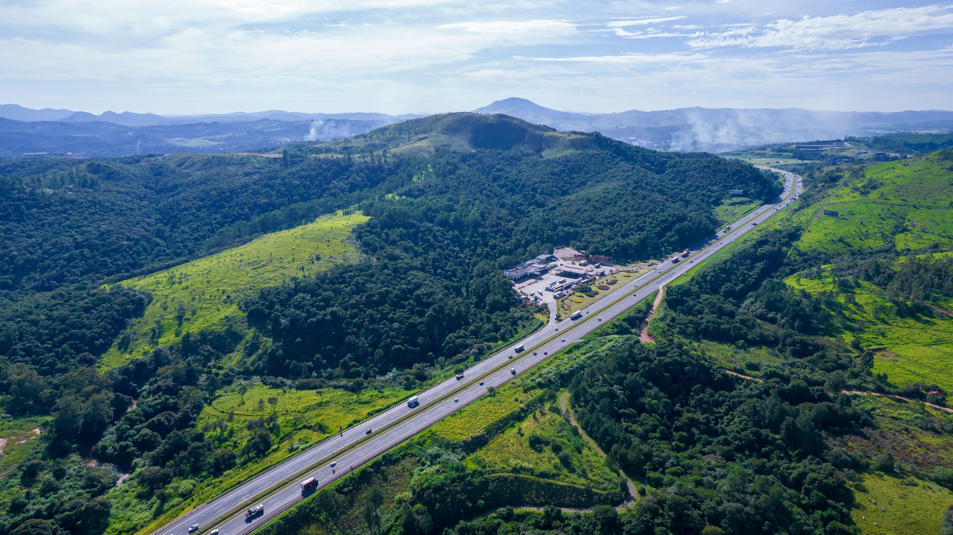 A highway winding through a lush green valley with a mountain range in the distance.