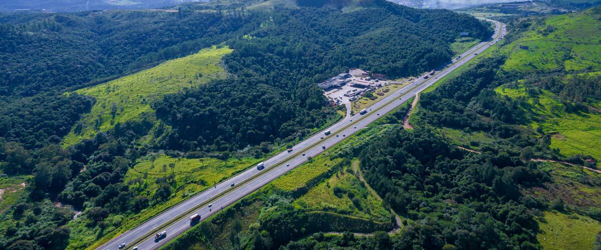 A highway winding through a lush green valley with a mountain range in the distance.