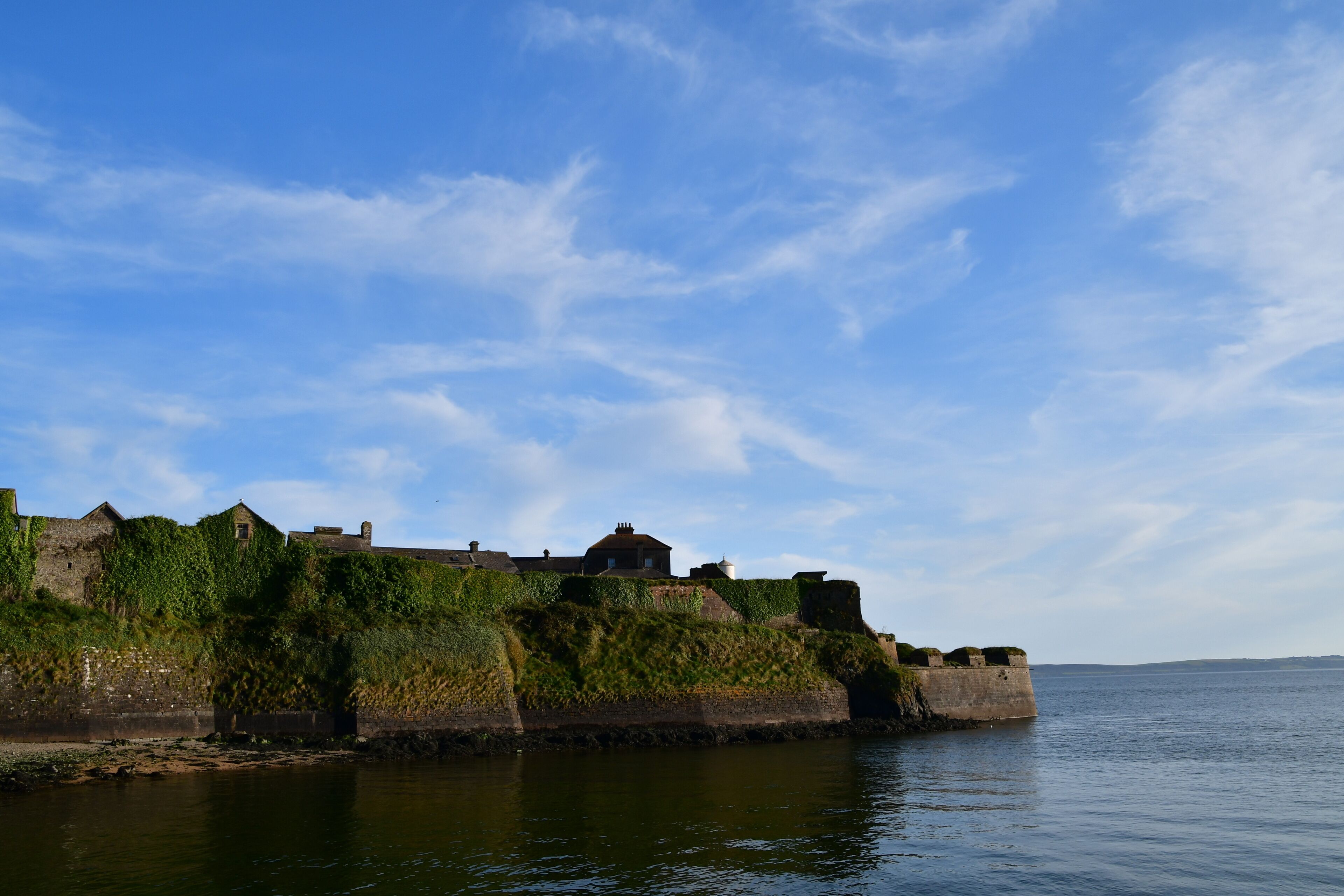 A coastal fortification with buildings on a grassy embankment overlooking the sea.