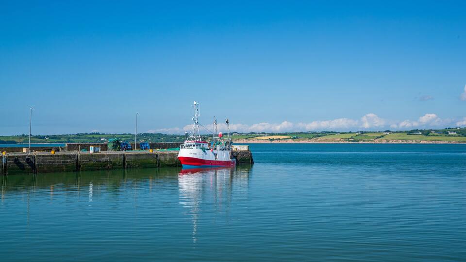 A red and white boat docked at a pier with calm water and a clear sky.