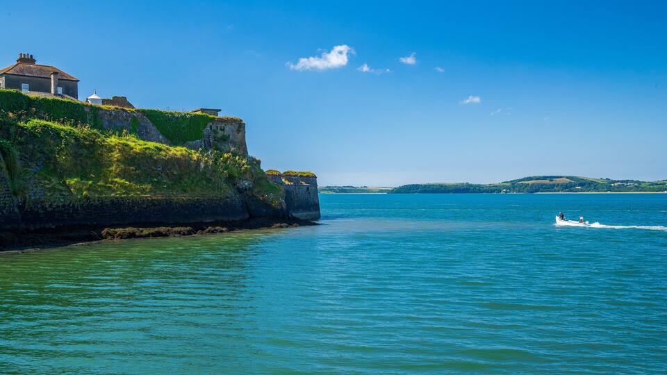 A coastal landscape with a cliffside building, calm sea, and a small boat in the distance.