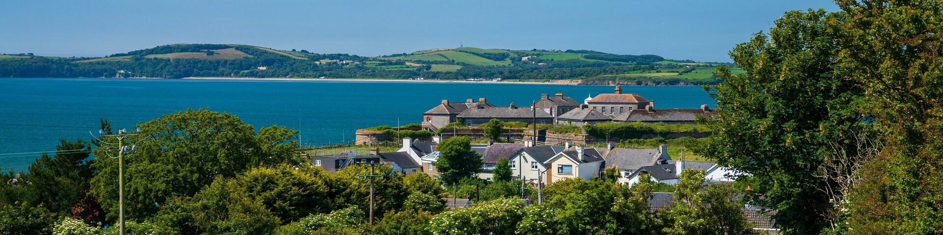 A coastal village with houses, a field, and a view of the sea and hills.