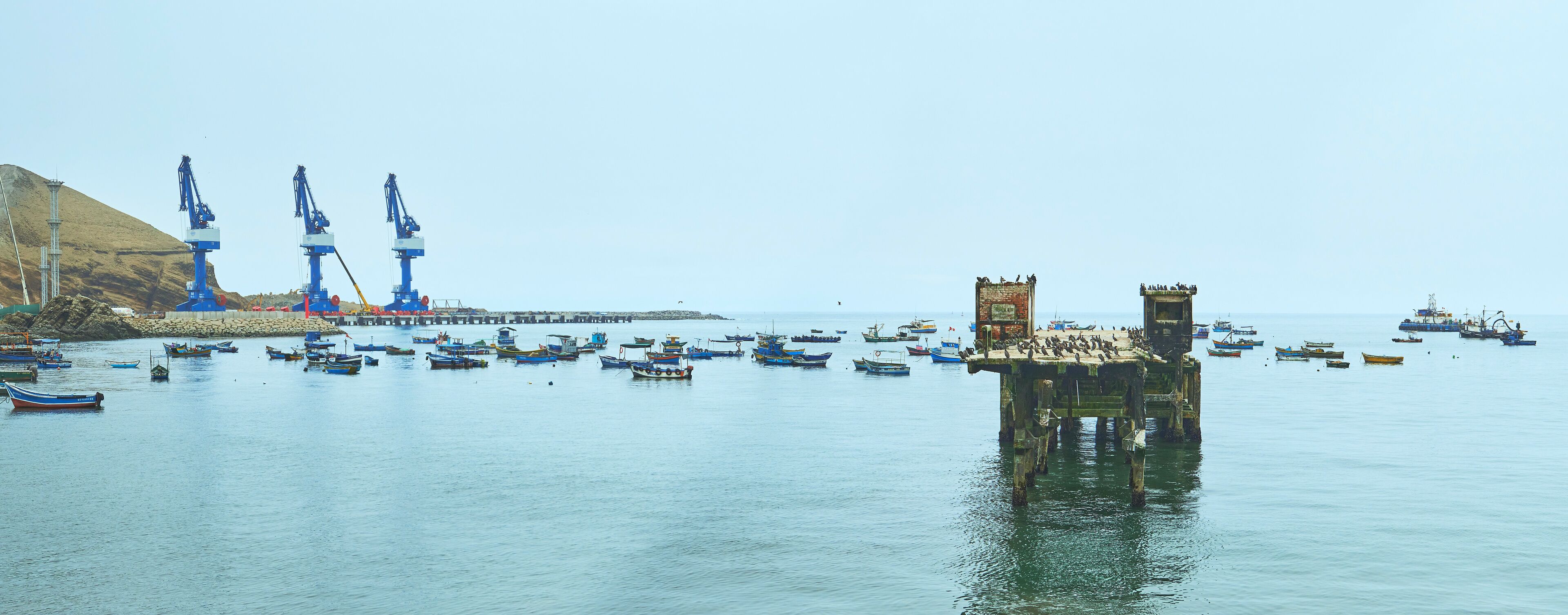A harbor with numerous boats, a pier with cranes, and a large tower.