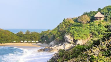 A beach with waves, umbrellas, and a thatched-roof building on a cliff.