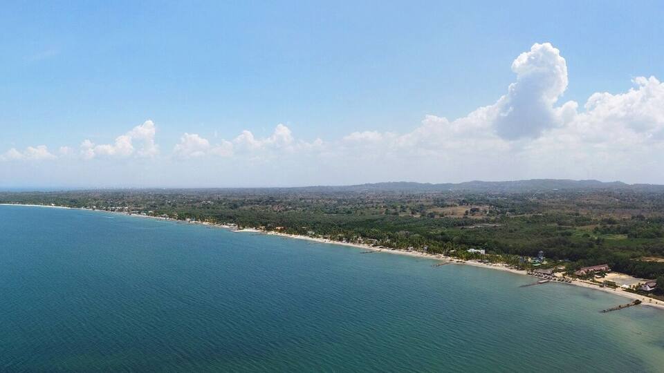 A coastal landscape with a clear view of the sea, a sandy beach, and a distant shoreline with greenery and buildings.
