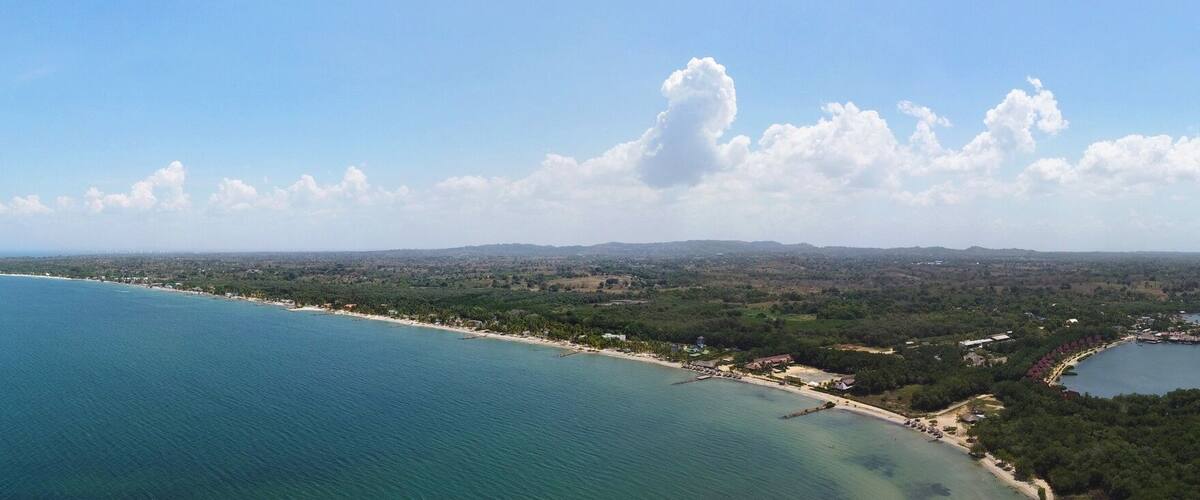 A coastal landscape with a clear view of the sea, a sandy beach, and a distant shoreline with greenery and buildings.